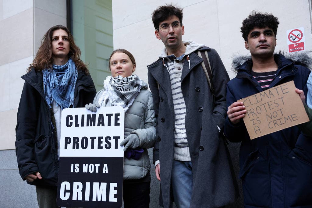 Greta Thunberg, ao lado de outros ativistas, segura cartaz com os dizeres 'Protesto climático não é um crime', durante seu julgamento em Londres (Foto: Reprodução/Internet)