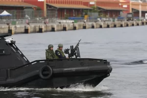 Imagem colorida mostra um barco de guerra com dois soldados no Rio de Janeiro
