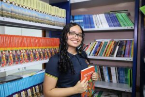 Imagem colorida mostra Raquel Nascimento na biblioteca de sua escola