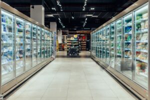Imagem colorida mostra um corredor de supermercado com refrigeradores